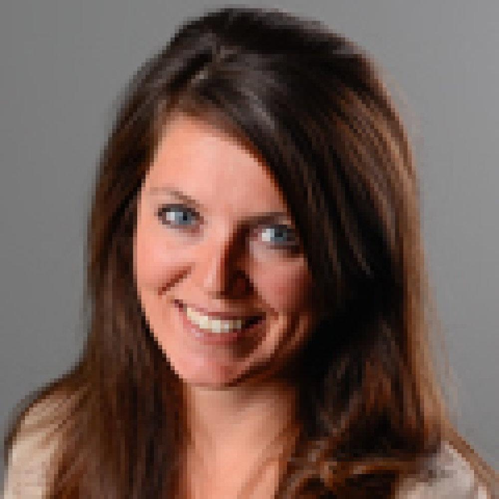 Lady with long dark brown hair with beige top in front of grey background